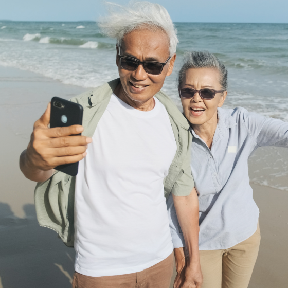 Older couple taking a selfie on the beach, happy that they've chosen the SecurePay Income benefit to meet their retirement goals.