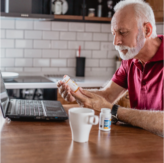 A man inspects a bottle of medication while sitting in front of a computer.