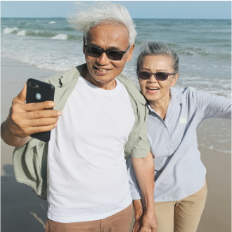 Older couple taking a selfie on the beach, happy that they've chosen the SecurePay Income benefit to meet their retirement goals